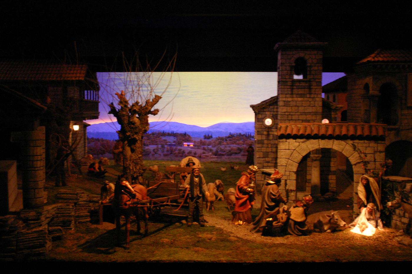 Il presepio del Natale 2007 al tramonto: un borgo di pietra con un carro, i Magi e la Natività sotto un arco; sullo sfondo le montagne.