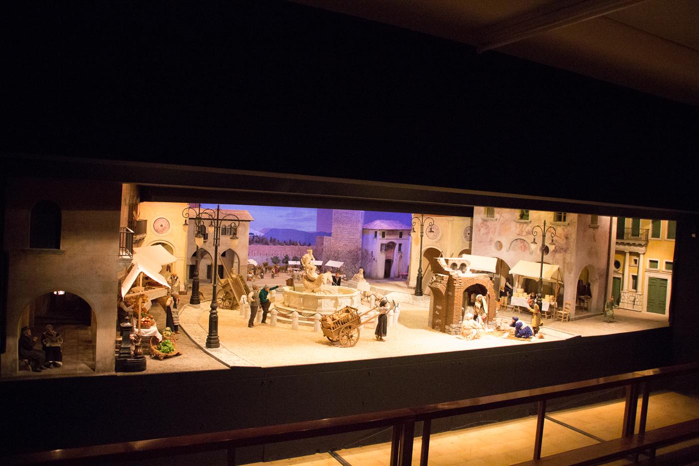 La sala del presepio nel Natale 2016, in luce di giorno: dietro la ringhiera, le case e la piazza di Conegliano in miniatura, con la fontana e la Natività sotto un arco di mattoni.