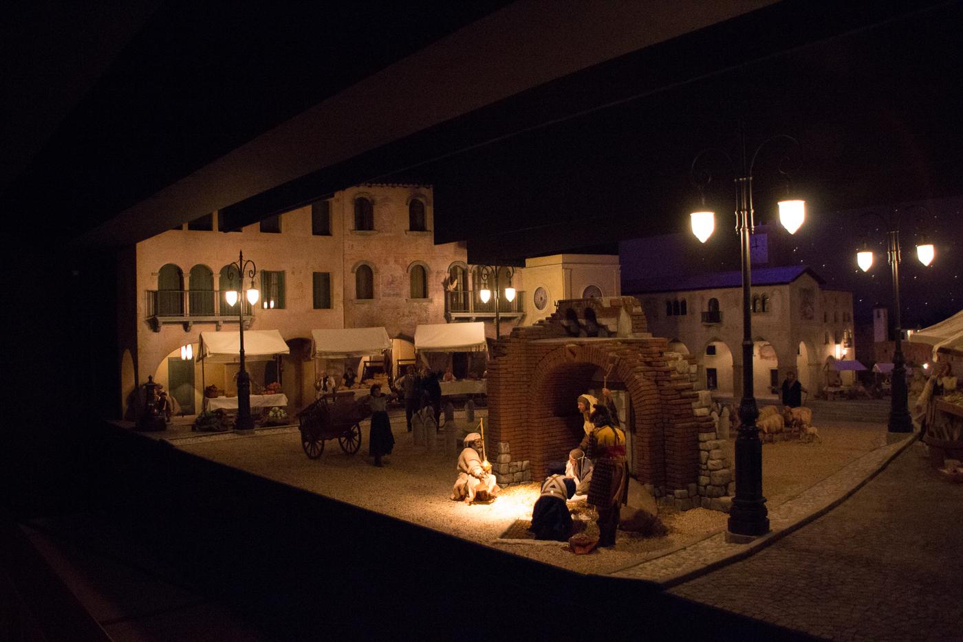 La sala del presepio al buio, nel Natale 2016: dietro la ringhiera, il paesaggio illuminato di Conegliano con le case, la piazza, il mercato e i lampioni accesi.