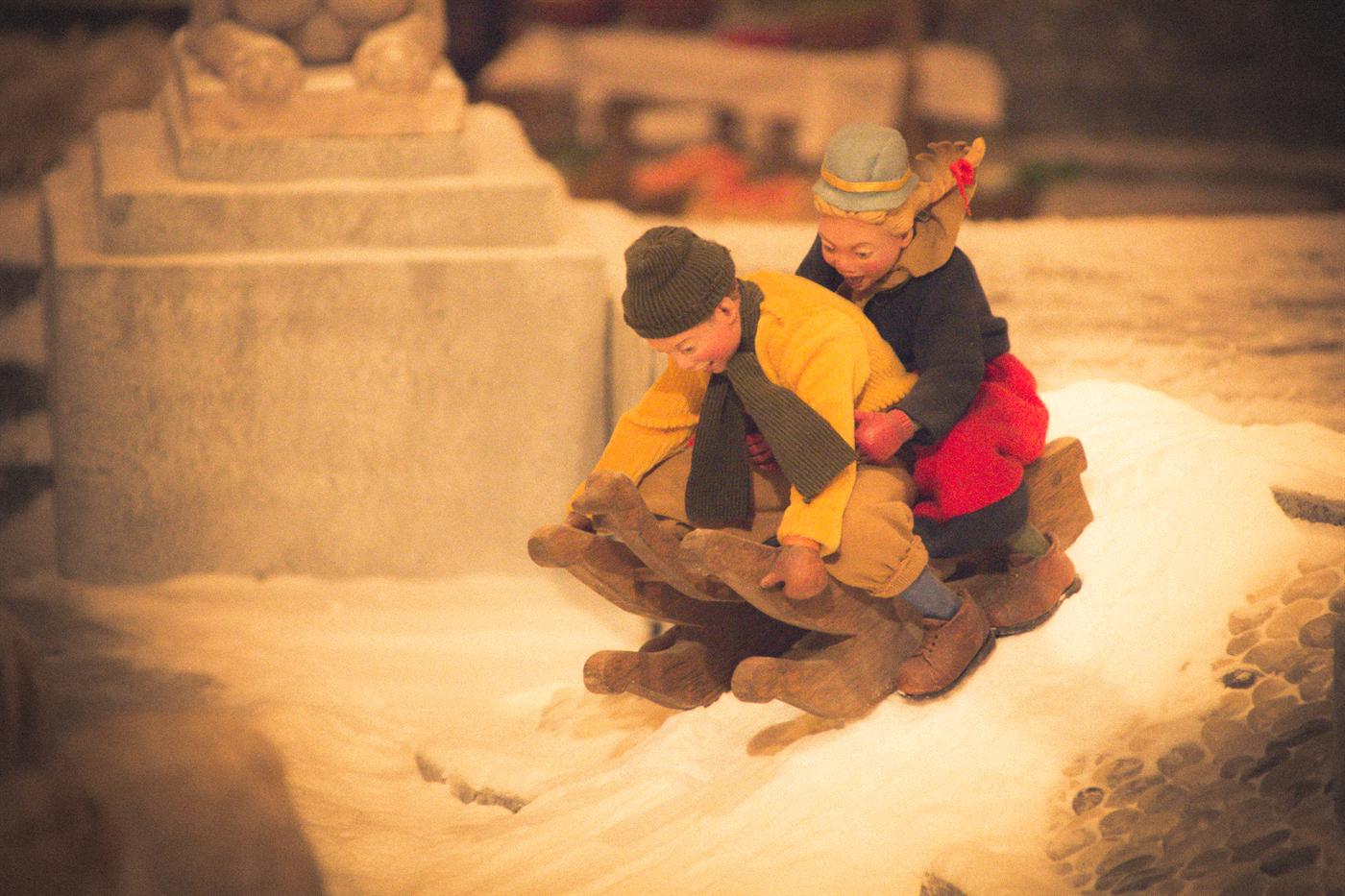Il presepio del Natale 2017: due statue di bambini con il cappello, seduti su una slitta di legno nella neve.