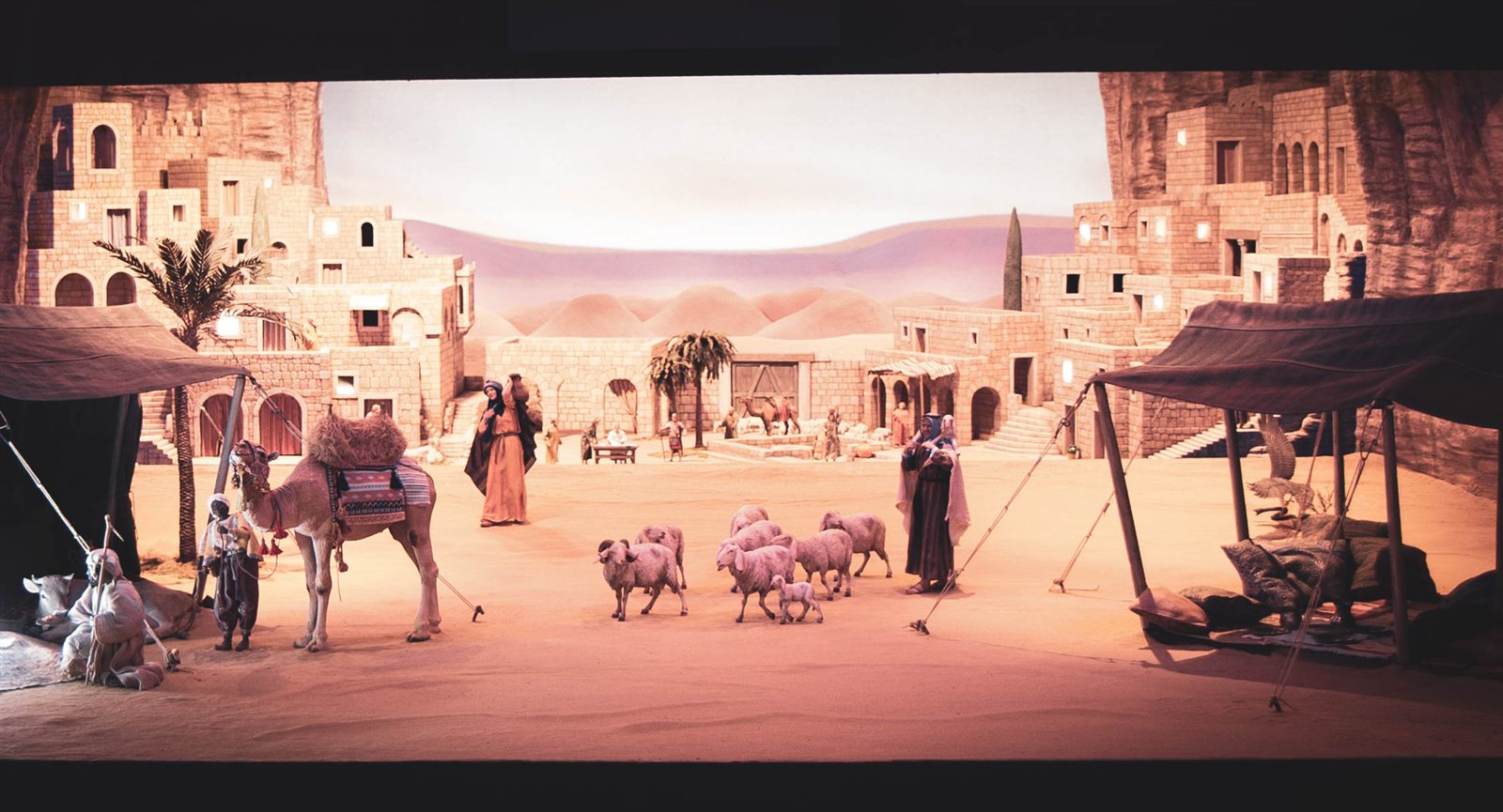 Natale 2022: un villaggio di pietra nel deserto, con le tende, un cammello, una donna con la brocca, un pastore e un gregge.